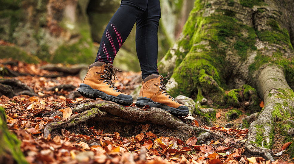 Leather hiking boot. Woman in leggings walks in the autumn woodland. Sports clothing